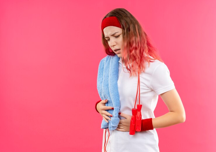 young-sporty-woman-headband-with-towel-shoulder-looking-tired-exhausted-touching-her-belly-standing-pink-wall_141793-50279