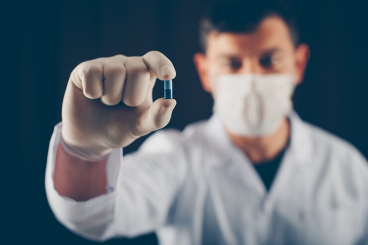 doctor-with-mask-gloves-holding-blue-pill-with-his-fingers-side-view_176474-1860
